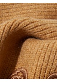 Tessuto a coste di colore giallo senape con una texture morbida. Presenta dettagli ricamati marroni in un motivo floreale. Aspetto caldo e accogliente.