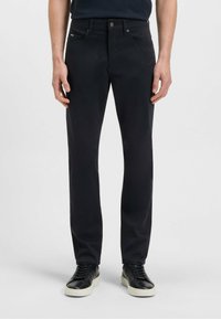 Svarta byxor med raka ben i slät tygkvalitet med framfickor, dragkedja och knappstängning samt diskret branding nära midjebandet.