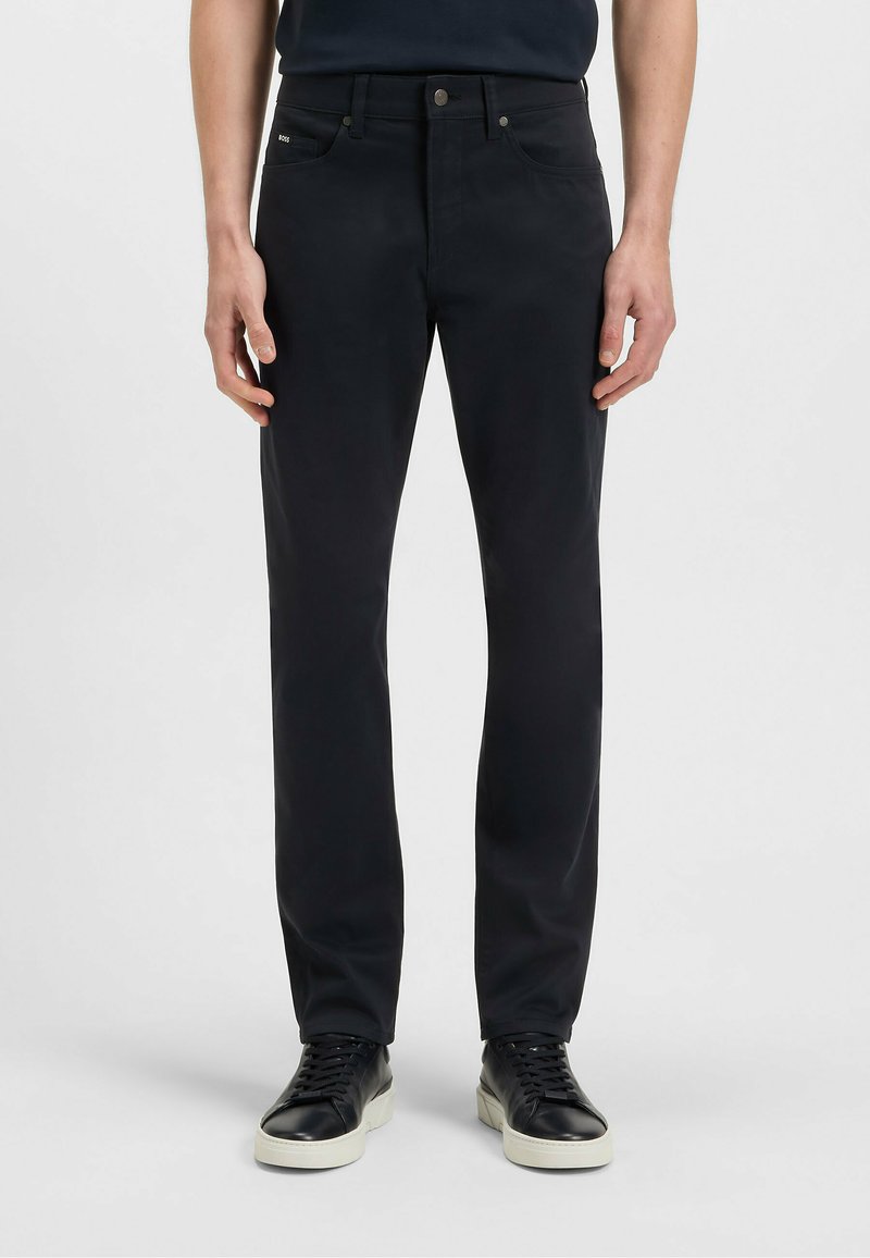 Svarta byxor med raka ben i slät tygkvalitet med framfickor, dragkedja och knappstängning samt diskret branding nära midjebandet.