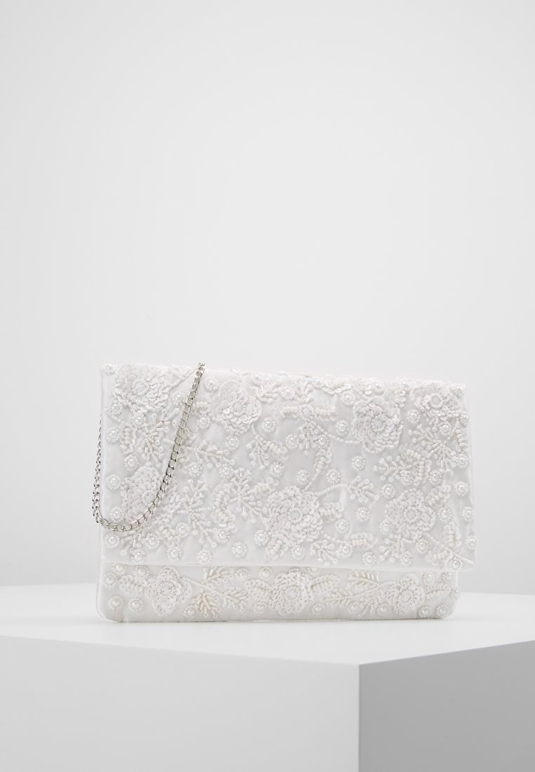 Pochette blanche avec broderie florale de perles et une bandoulière chaîne argentée sur un piédestal blanc dans un fond uni.