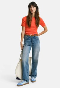 Lys orange ribbet strikket kortærmet top, høj talje falmede blå brede bukser, blå og hvide sneakers, tan læderbælte og stor tote taske.