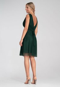 Grünes, ärmelloses Kleid mit V-Ausschnitt und Bindeband in der Taille. Hergestellt aus einem leichten Material, mit einem fließenden Rock und transparenter Saum.