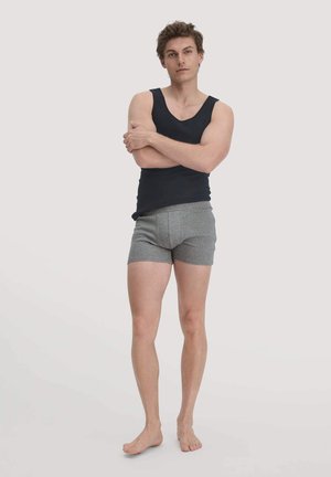 Schwarzes Tanktop und graue Boxershorts an einem stehenden männlichen Modell. Das Top ist ärmellos und die Shorts sind körpernah geschnitten mit einer glatten Textur.