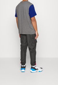 Grå og blå farveblokeret t-shirt, cargo bukser i mørkegrå, og sort-hvide sneakers med blå accenter. Simpelt design, afslappet pasform.