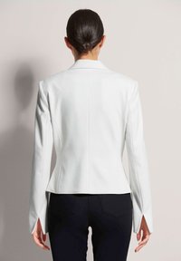 Weißes maßgeschneidertes Blazerjackett mit taillierter Silhouette, langen Ärmeln und strukturiertem Schulterdesign; Rückenbelüftung verbessert die Bewegungsfreiheit.