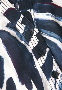 Chemise avec un motif abstrait en marine, noir et blanc. Elle possède des boutons noirs et des coutures détaillées le long de la patte de boutonnage.