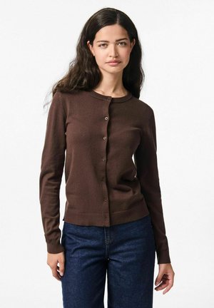 Cardigan marron à manches longues avec un col rond, fermeture à boutons et ourlet côtelé. Texture douce, design ajusté, porté avec un jean en denim sombre.