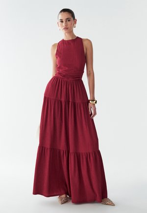 Maxi dress in deep red, featuring a fitted bodice, gathered waist, and tiered skirt. Made of textured fabric, with a sleeveless design.