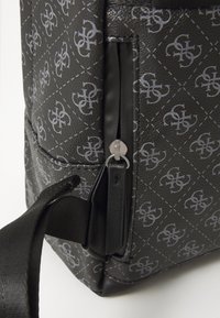 Sac à dos noir à motifs avec un extérieur texturé, un design de logo gris, une poche zippée et des sangles en tissu durables.