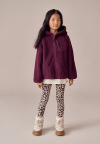 Lilla fleecetrøje med hætte og lynlås foran samt forlommer, kombineret med leopardmønstrede leggings og beige støvler foret med pels.