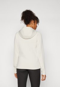 Haut à capuche gris clair avec capuche, manches longues et coupe ajustée. Texture douce et lisse avec un ourlet qui descend jusqu'à la taille.