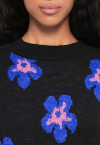 Zwarte trui met een gebreide patroon van grote blauwe bloemen met roze centra. De stof lijkt zacht en gestructureerd, met een ronde hals.