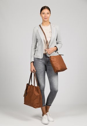 Bruine leren tote bag met dubbele handvaten en een kwastdetail; kleinere bruine leren crossbody bag; grijze blazer en lichte top gedragen met jeans.