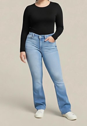 Persoon draagt een strakzittend zwart shirt met lange mouwen, lichtblauwe jeans met hoge taille en een lichte uitlopende pijp, en witte sneakers, staat met één hand in de zak.