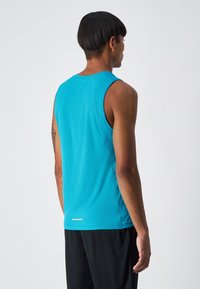 Sportowa bezrękawnik w jasnoniebieskim kolorze, wykonana z teksturowanej tkaniny. Posiada okrągły dekolt i mały odblaskowy detal na dolnym brzegu.