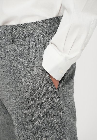 Grau strukturierte Hose mit dezentem Muster, ausgestattet mit einer Seitentasche und einem flachen Bund, kombiniert mit einem weißen Hemd mit Kragen.