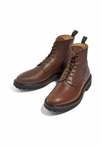 Botas de tobillo de cuero marrón con un acabado texturizado, que cuentan con un diseño de cordones, punta redonda y una suela de goma duradera. Incluyen lengüetas para facilitar el calzado.