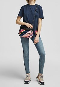 Värikäs käsilaukku, jossa on vaaleanpunaisia, sinisiä ja keltaisia raitoja, mustalla kahvalla ja ketjuyksityiskohdalla, käytössä henkilöllä rento vaatetus.