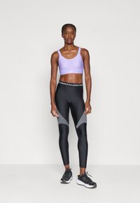Purpurs sportsa krūšturis ar regulējamām siksnām, apvienots ar melnām leggings ar pelēkiem akcentiem un melnu jostu. Melni sporta apavi.