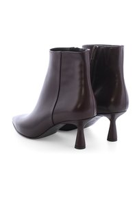 Bruine leren enkellaarsjes met spitse neuzen, een glanzende afwerking, ritssluiting en unieke flare hakken. Soepele textuur met minimale stikseldetails.