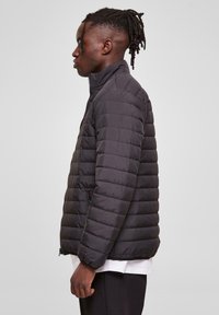Black quilted puffer jacket with a high collar, front zipper, and side pockets, featuring a smooth, shiny texture and structured silhouette.