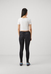 Black skinny jeans with a sleek design, featuring two back pockets, and a white short-sleeve top. Fabric appears smooth and fitted.