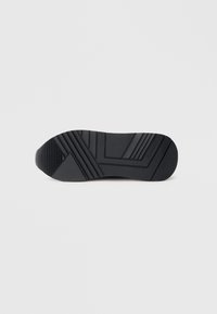 Czarna gumowa podeszwa buta z geometrycznymi wzorami bieżnika i napisem "GUESS" wytłoczonym w pobliżu pięty na białym tle.