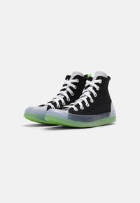 Zapatillas altas con parte superior de lona negra, cordones blancos, protector de goma transparente en la punta y suela verde. Cuenta con ojales reforzados.