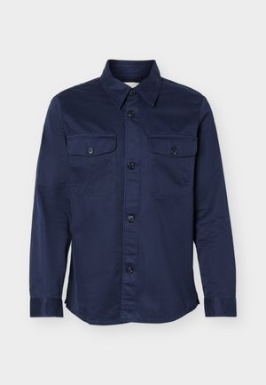 Μπλε σκούρο πουκάμισο με μακριά μανίκια, κουμπιά στο εμπρός μέρος και δύο τσεπάκια στο στήθος με κουμπιά, εμφανίζεται σε λευκό φόντο.