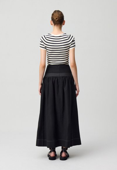 Haut ajusté noir et blanc rayé associé à une longue jupe noire froncée, avec une taille lisse et des coutures blanches contrastantes.