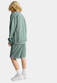 Grøn sweatshirt og matchende shorts lavet af blødt stof. Sweatshirten har en afslappet pasform og kontrasterende syninger; shortsene har et pink label.