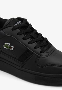 Zapato deportivo negro hecho de cuero liso, con puntera redonda, panel texturizado, cordones planos y un pequeño logo bordado de cocodrilo.