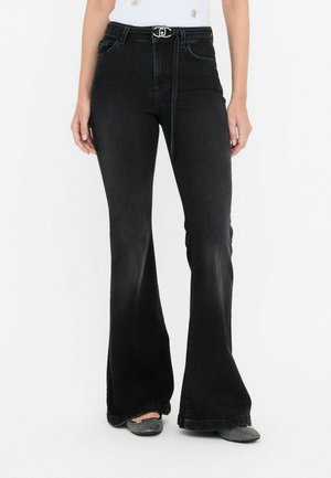 Black flared jeans with a high waist, featuring a metallic belt buckle, front pockets, and a faded texture, paired with patterned shoes.