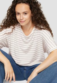 Gestreiftes T-Shirt aus weichem, weißem Stoff mit helllila Streifen, entspannte Passform, kurze Ärmel und runder Ausschnitt. Getragen mit blauen Jeans.