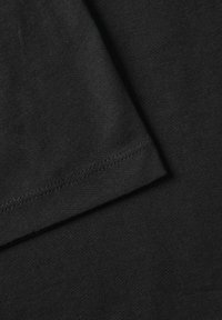 Tessuto di cotone nero con una consistenza liscia, vista ravvicinata del bordo di una manica e dettagli di cucitura ordinati.