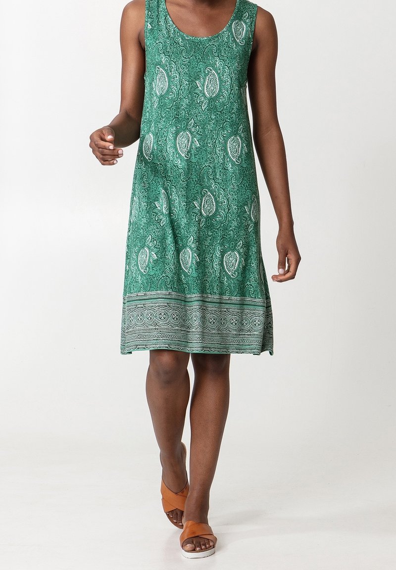 Robe verte sans manches avec un motif cachemire, un col rond et un ourlet texturé orné d'une bande décorative. Portée avec des sandales marron.