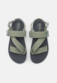 Green fabric sandals with adjustable straps, textured black sole, and logo detailing. Crossed straps provide secure fit for outdoor use.