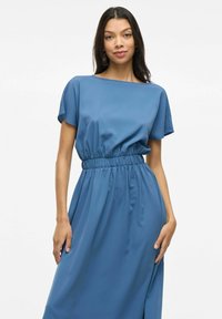 Rochie albastră, cu mâneci scurte, dintr-un material neted; dispune de un brâu elastic și are o siluetă fluidă. Design simplu, relaxat.