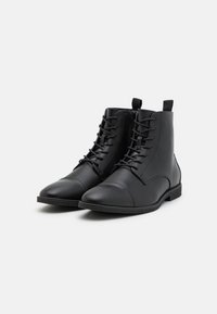 Bottes cheville en cuir noir avec un bout arrondi, fermeture à lacets à l'avant et semelle texturée. Elles présentent une finition lisse et une languette à l'arrière.