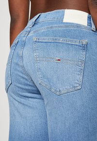 Vaqueros de mezclilla azul claro con un diseño ajustado, que cuentan con un parche del logo de Tommy Jeans en la cinturilla y un pequeño logo en el bolsillo trasero.