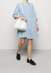 Blå och vit rutmönstrad klänning med trekvartslång ärm, flertrapsdesign och rund halsringning; matchad med en vit bucket bag och svarta skor.