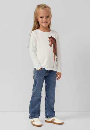 Witte longsleeve shirt met een afbeelding van een bruine paard, gecombineerd met blauwe denim jeans en crèmekleurige sneakers met bruine accenten.