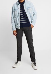 Světle modrá džínová bunda, tmavě modrý pruhovaný pletený svetr, tmavě šedé kalhoty a bílé tenisky s černými detaily. Ležérní vrstvení a čisté linie.