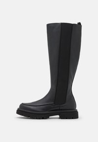 Bota negra hasta la rodilla con cuero liso y paneles laterales elásticos, punta cuadrada, suela gruesa y tirador en la parte posterior.