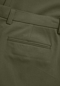 Olívazöld nadrág sima textúrával, egyetlen hátsó zsebbel és lapos derékpánttal, amelyen övhurkok találhatók.