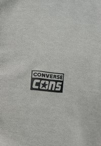 Γκρι ύφασμα με μαύρο λογότυπο "CONVERSE CONS" που περιλαμβάνει ένα αστέρι μέσα στο γράμμα "O" της λέξης "CONS".