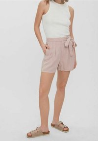 Ljust rosa högmidjade shorts med ett knytbart bälte, två sidofickor och mjuk textur. Kombineras med en vit ärmlös topp och beige sandaler.