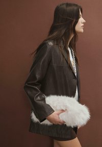 Brun læderjakke, hvid faux fur clutch med kæde-rem, glat overflade og en slank silhuet mod en brun baggrund.
