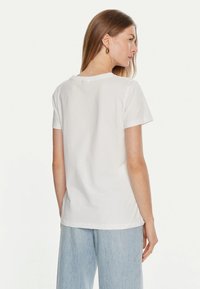 T-shirt bianco a maniche corte realizzato in cotone, con vestibilità rilassata, caratterizzato da un colletto rotondo e una texture morbida. Indossato con pantaloni a gamba larga azzurri.
