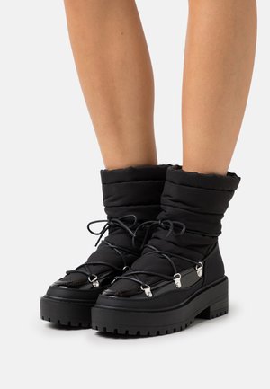 Bottes d'hiver noires avec un dessus matelassé, fermeture en dentelle et semelle en caoutchouc épaisse. Présente des accents brillants et une finition texturée.